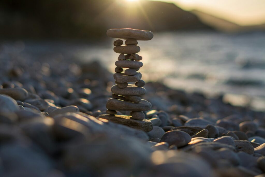 A balanced stack of smooth stones on a beach at sunset, symbolizing mindfulness, balance, and the calm found through practicing radical acceptance.