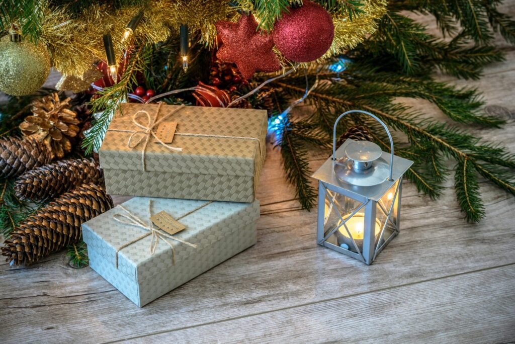 Holiday season decorations with wrapped gifts, pinecones, ornaments, and a lit lantern under a Christmas tree, creating a warm and festive atmosphere.