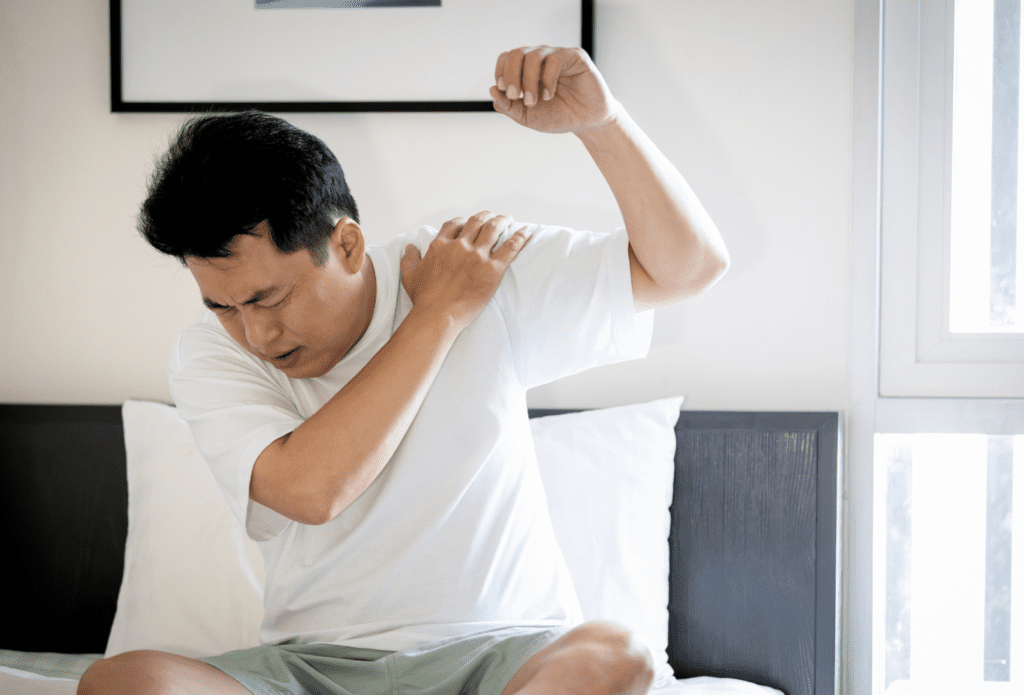 Man experiencing sharp shoulder pain while lifting his arm, illustrating common symptoms of shoulder impingement.