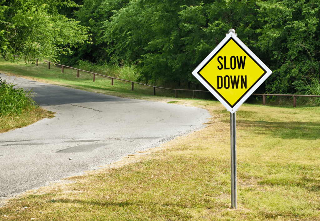 Yellow road sign reading “Slow Down” along a quiet road, symbolizing slowing down when feeling overwhelmed and needing space to reset.
