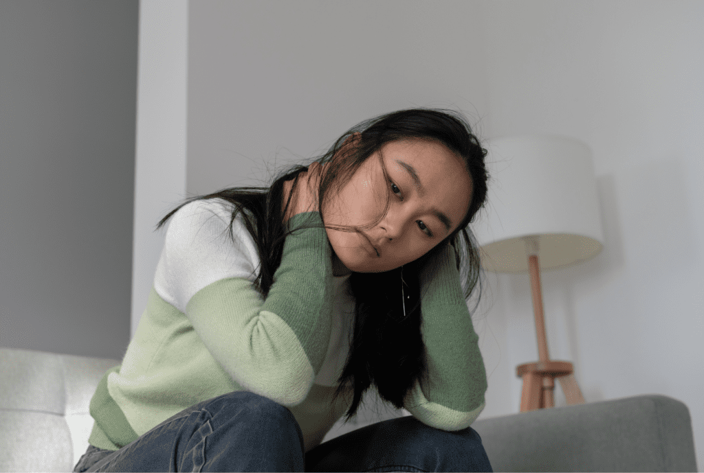 A woman sitting alone on a couch with her head resting in her hands, reflecting the emotional weight of being the different one in her family.