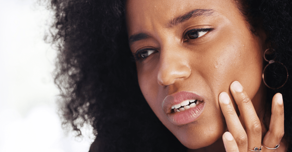 Woman holding her jaw in pain, illustrating TMJ dysfunction and jaw tension linked to chronic headaches.