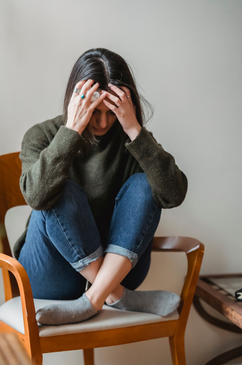 Young woman sitting curled up in a chair appearing distressed, representing how anxiety can feel mentally and physically overwhelming.