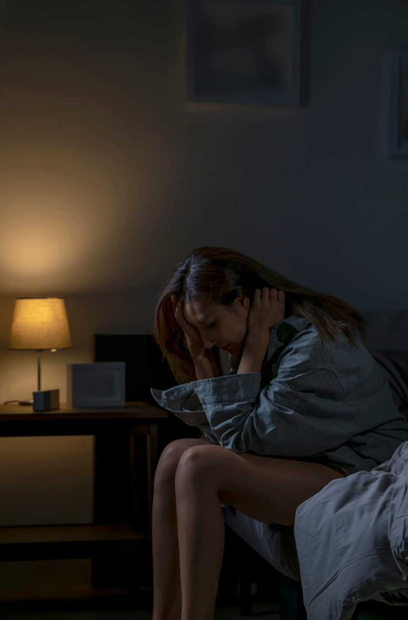 Woman sitting on bed at night holding her head, reflecting insomnia and distress linked to depression.