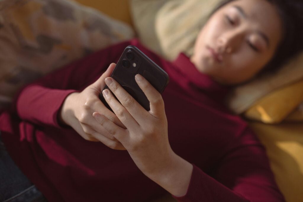 Woman lying on a couch scrolling on her phone late at night, illustrating social media use and mental health impact.