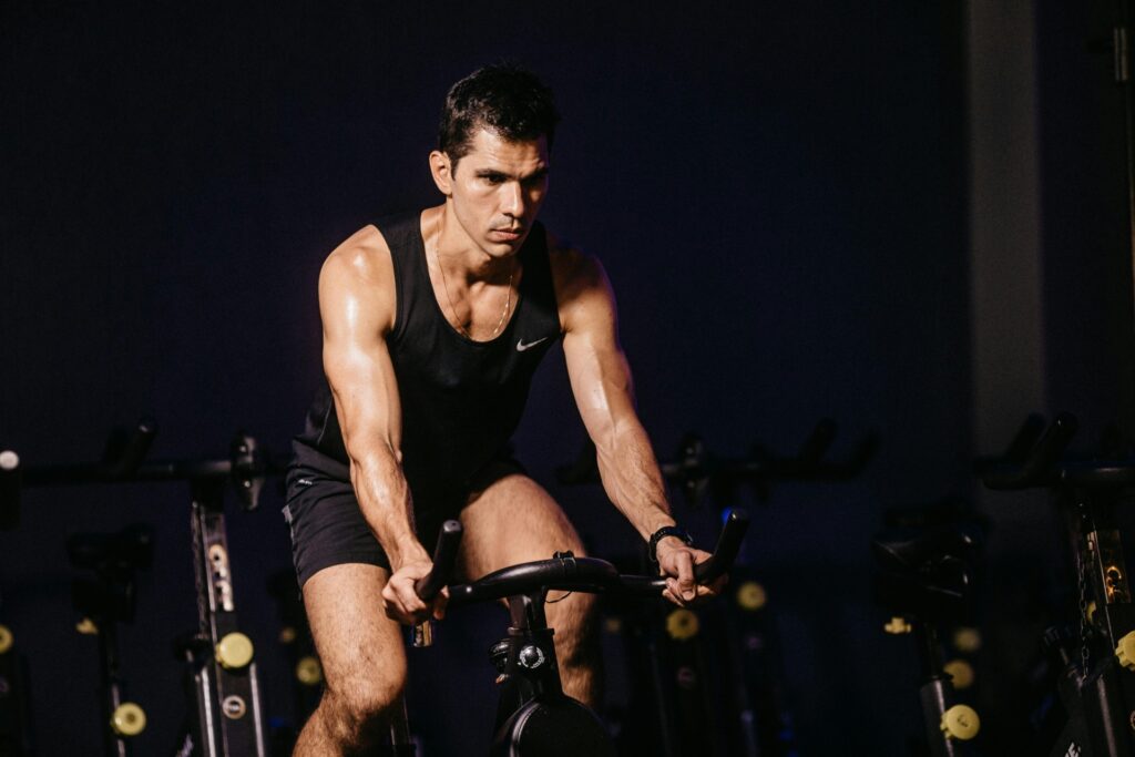 Man doing cardio workout on a stationary bike in a dimly lit gym.