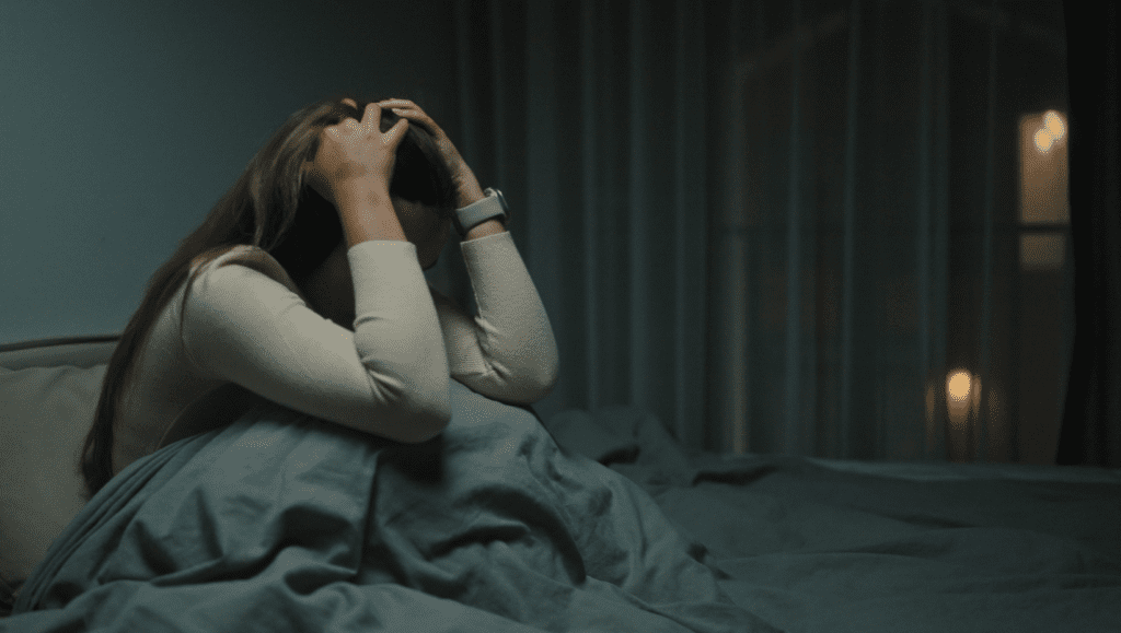 Woman sitting awake in bed at night with her head in her hands, illustrating nighttime anxiety and emotional overwhelm.