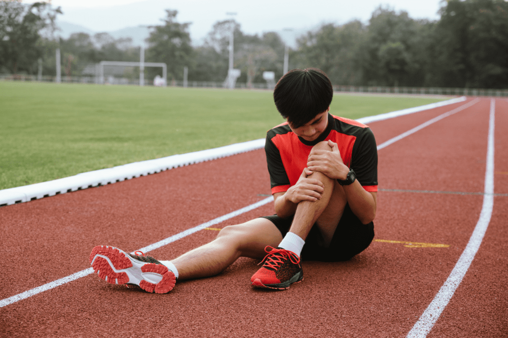 Athlete sitting on a running track with patellar tendinopathy knee pain after training, showing patellar tendon irritation and sports-related knee discomfort.