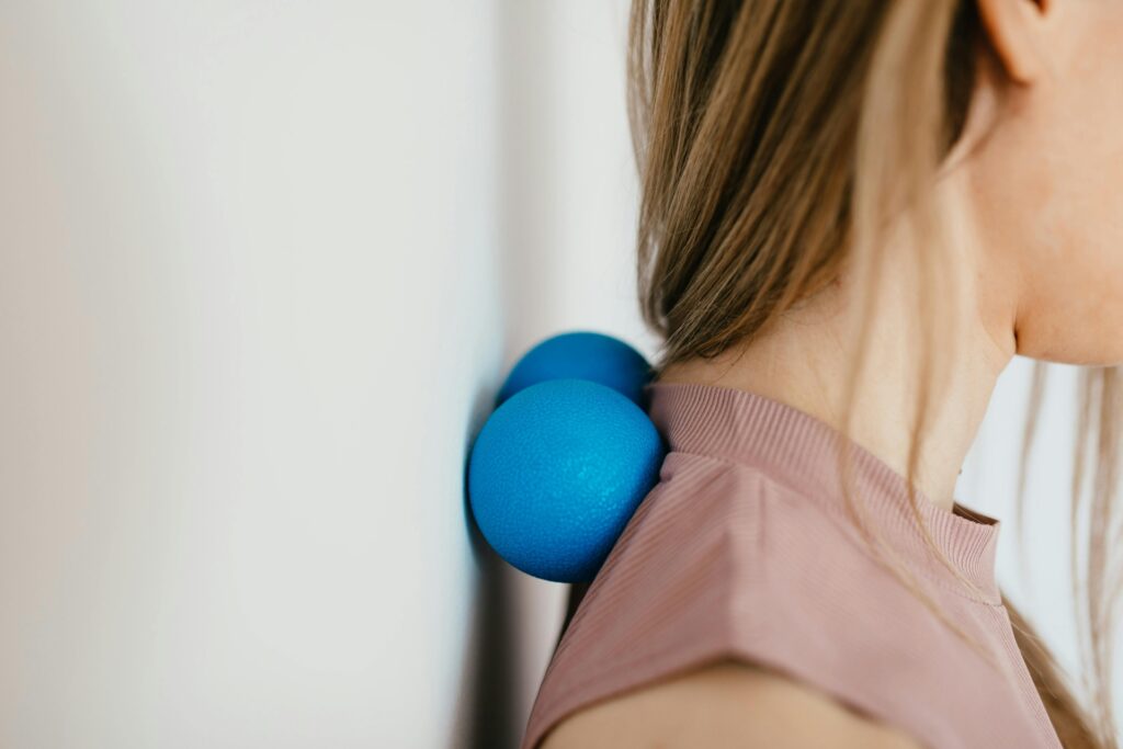 Person using a massage ball on the upper neck and shoulders for cervicogenic headaches relief, targeting neck tension and headache-related muscle tightness.