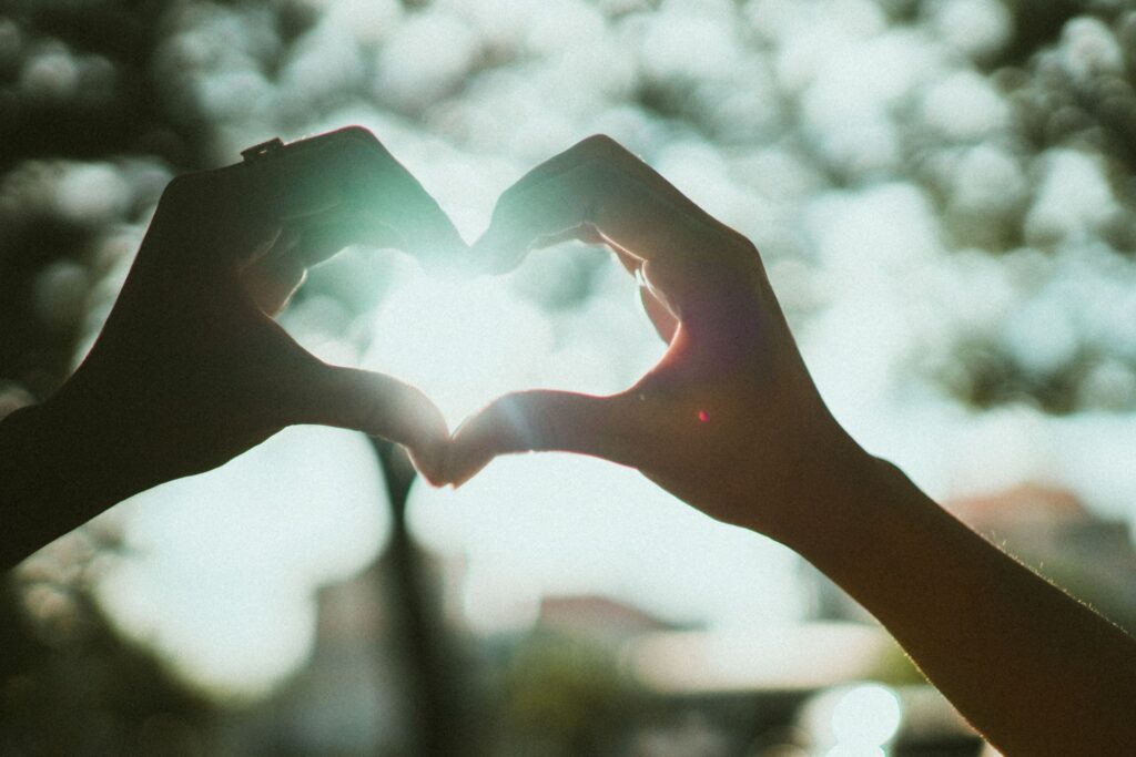 Hands forming a heart shape in the sunlight, symbolizing healing, hope, and recovery after trauma.