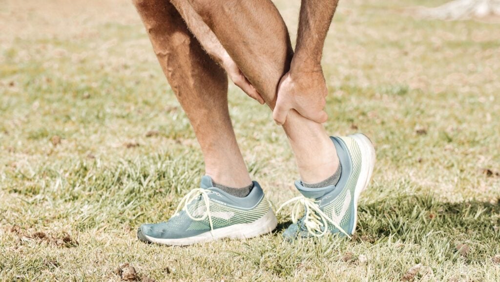 Person holding the back of their heel while experiencing pain associated with Achilles tendinopathy.