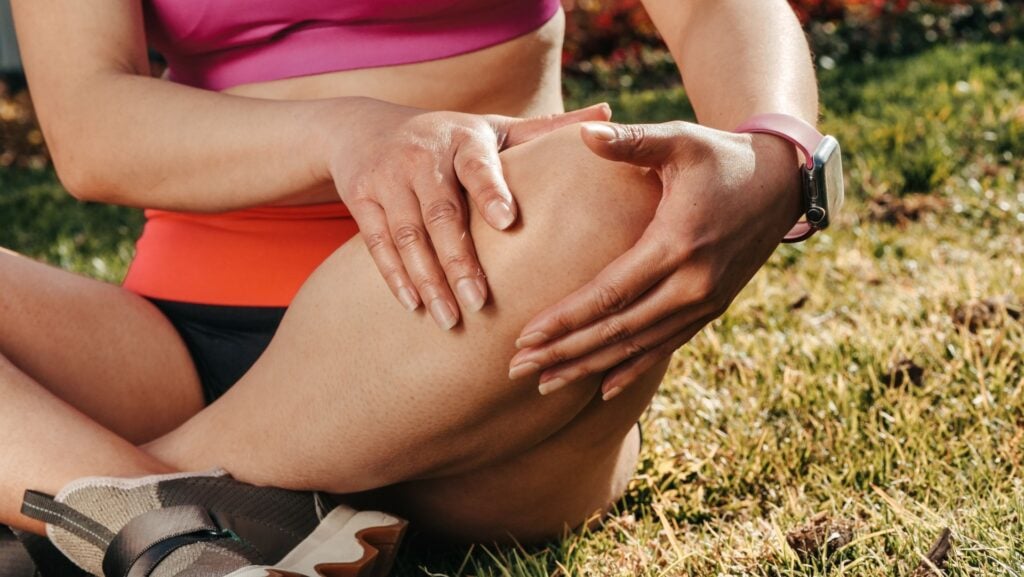 Woman holding her knee while sitting outdoors with pain related to patellar tendinopathy.