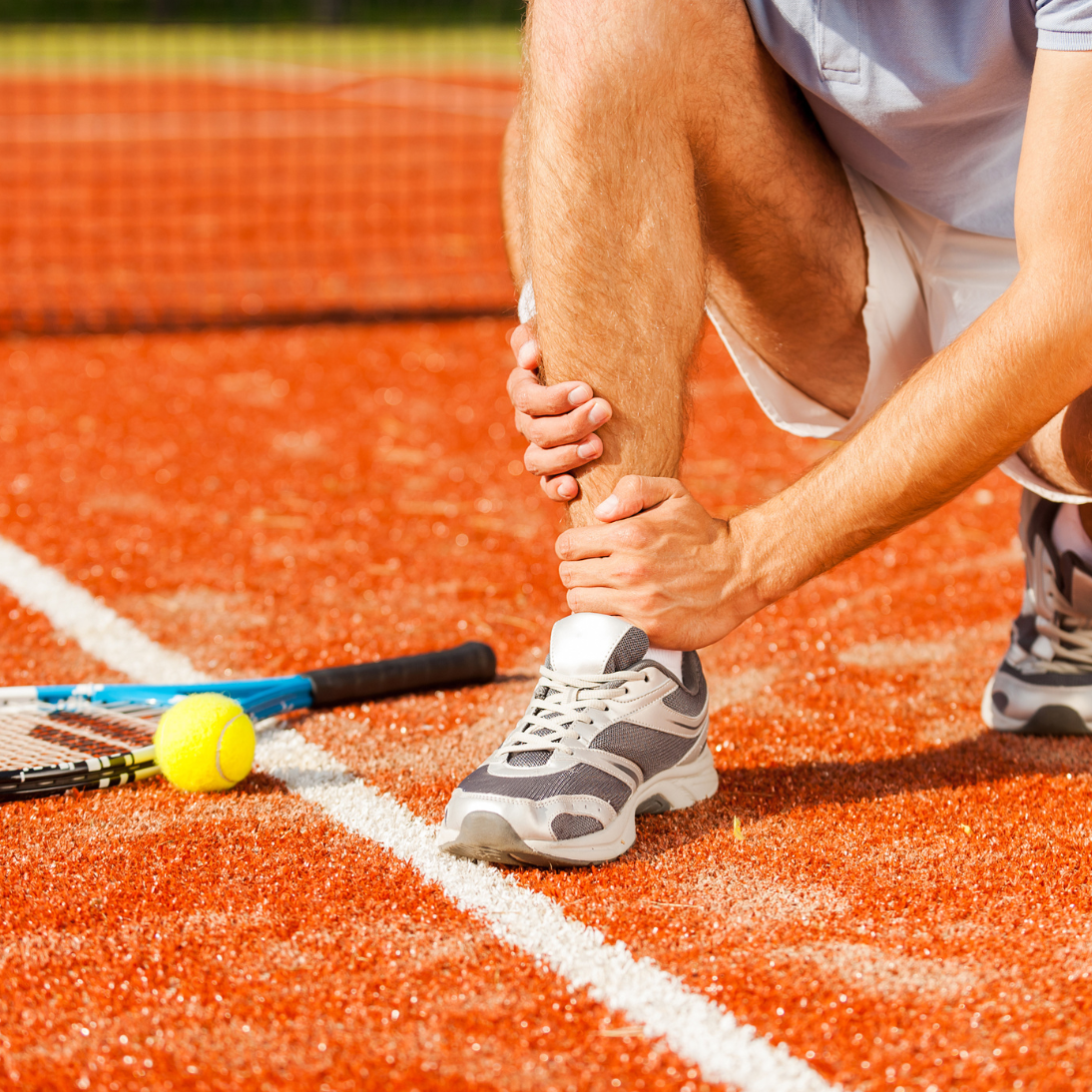 Tennis player holding ankle in pain on the court after a sports injury during play.