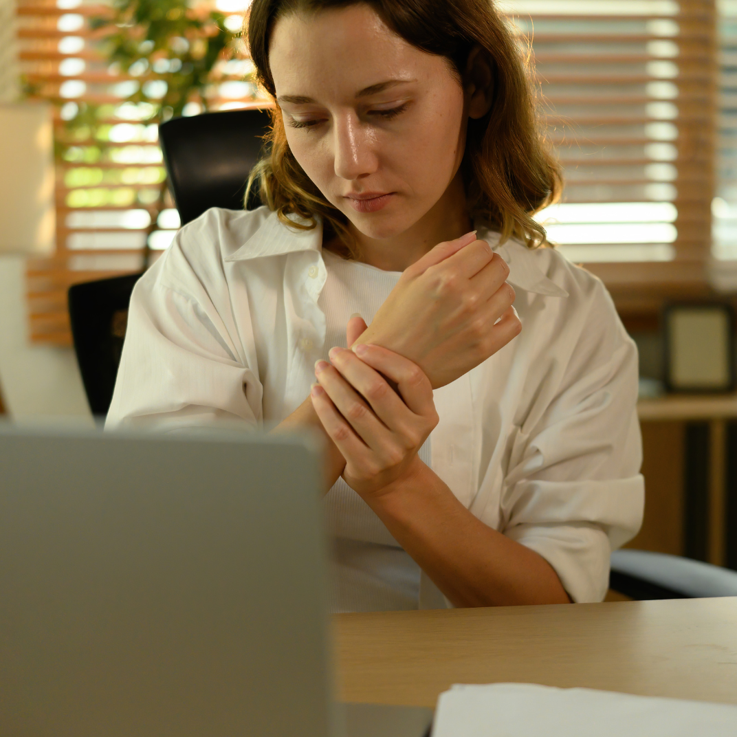 Woman experiencing wrist pain while working at a computer, a common symptom of carpal tunnel syndrome.