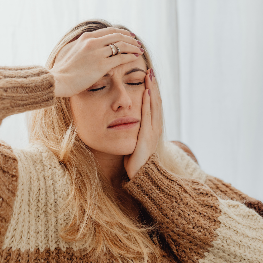 Woman holding her forehead in pain due to headaches and migraine symptoms.