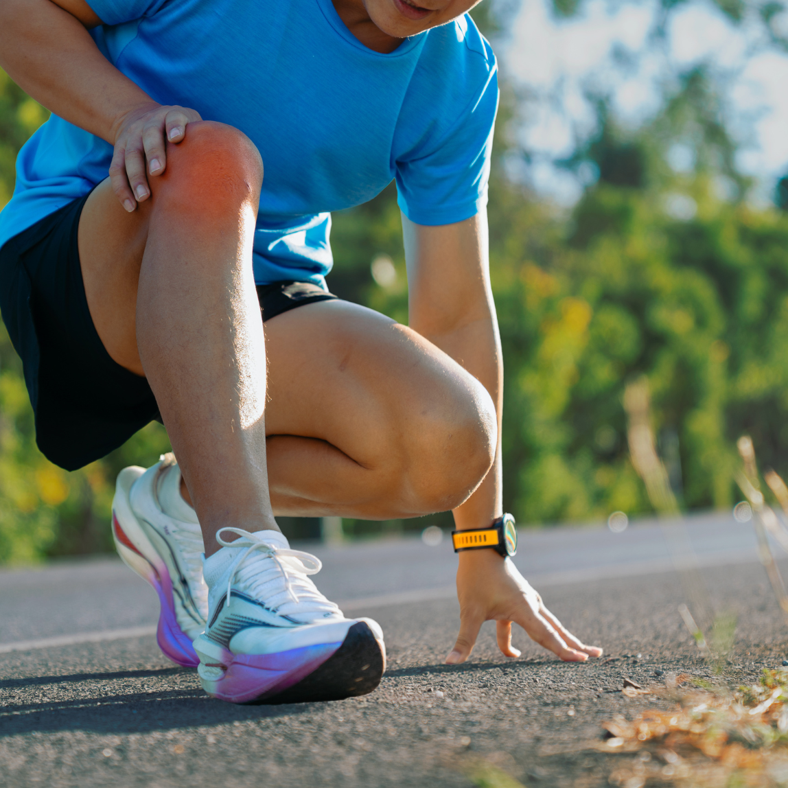 Runner experiencing knee pain from sports injuries while stretching on a roadside trail.