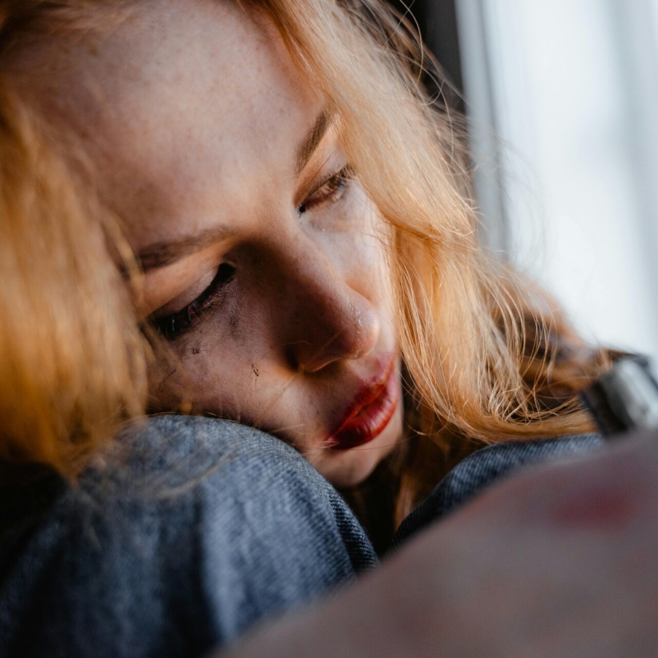 Woman leaning against window with tearful expression, reflecting emotional trauma and isolation.